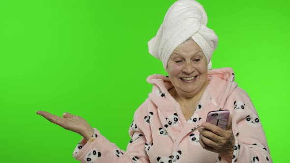 Elderly Grandmother in Bathrobe. Old Woman with Smartphone Pointing at Something