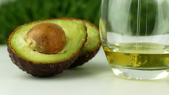 Pours avocado oil into a glass next to the avocado. 4K video close-up of healthy food.