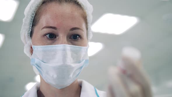 Female Doctor in a Face Mask is Looking at a Medicine Tub