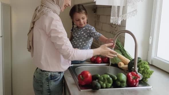 A Young Beautiful Mother in Hijab and Her Little Daughter Wash Vegetables Under the Tap with Water