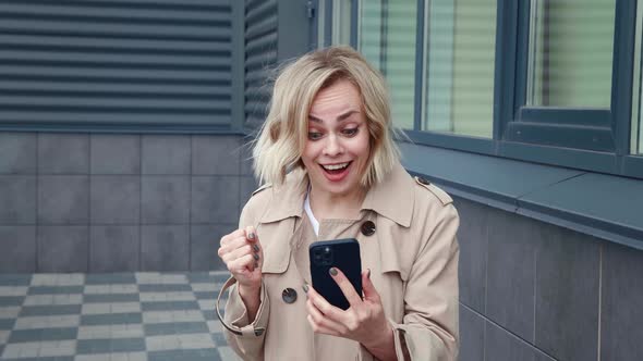 Portrait of Happy Business Woman Enjoy Success Win on Smartphone While Standing Outdoors in Downtown