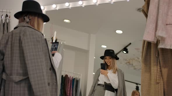 Stylish Young Woman Taking Selfie in Fitting Room Against Big Mirror of Modern Boutique