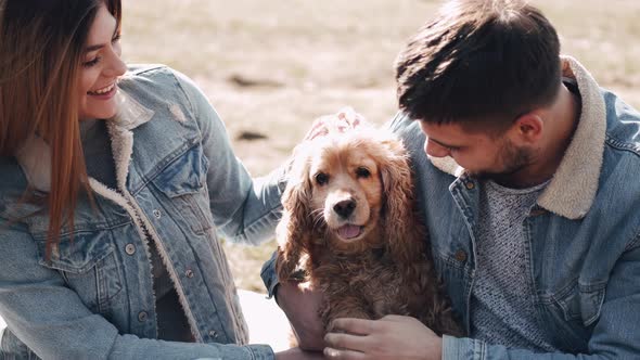 Pretty Young Woman and Man Are Sitting in the Field Walking with a Cute Dog