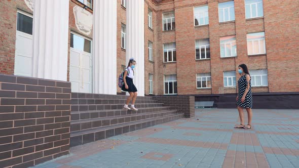 Mom Meets Daughter From School in Schoolyard. Schoolgirl, with Backpack, and Woman, Are Both in