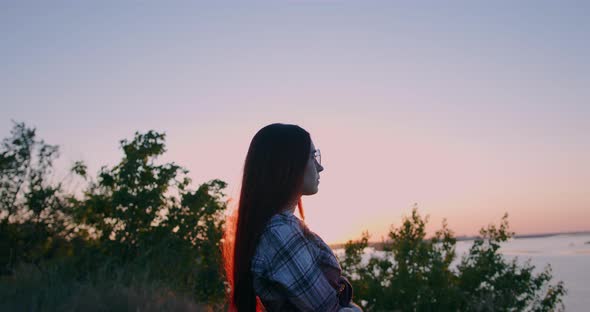 A young girl on the background of sunset looks thoughtfully into the distance