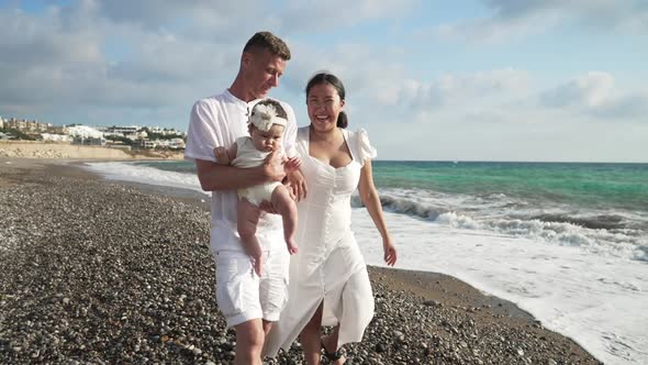 Portrait of Happy Young Caucasian Man and Asian Woman Walking with Cute Baby Girl in Slow Motion