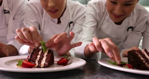 Line of Chefs Garnishing Dessert Plates with Mint Leaves and Strawberries