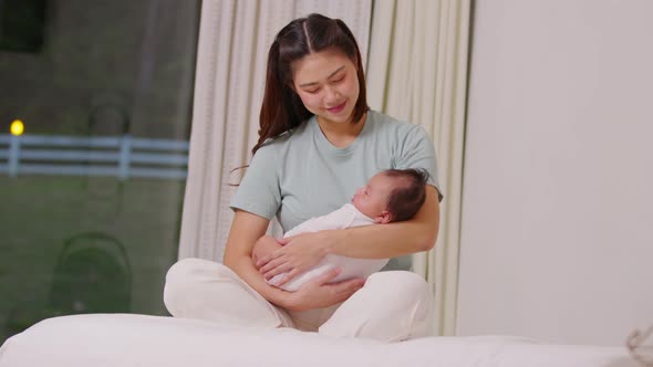 Beautiful Asian mom woman holding newborn baby in her arms sit on bed at white cozy home