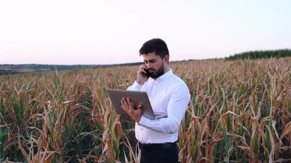Young Businessman Analyzes a Laptop Irrigation Plan and Talks on the Phone for More Directions.