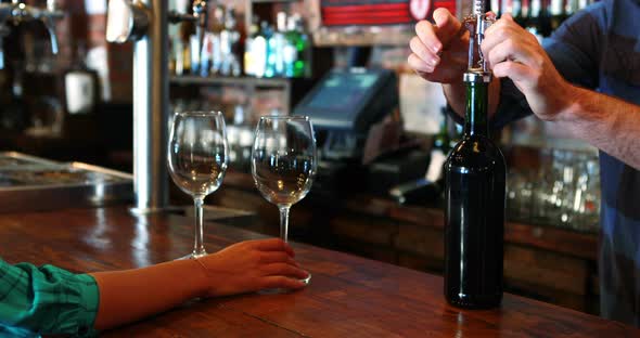 Barman opening wine bottle with corkscrew at bar counter