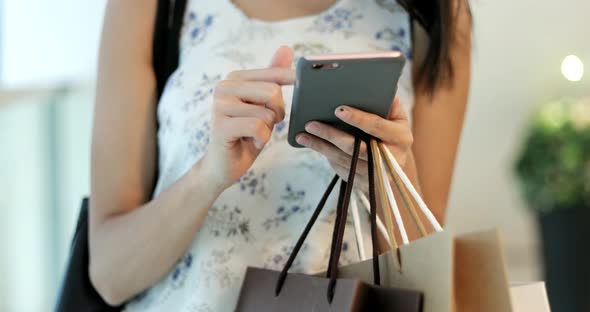 Woman using smart phone and holding shopping bag