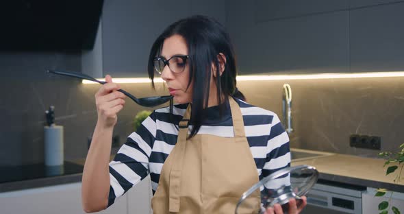 Brunette in Glasses Preparing Soup and Tasting it from Spoon and Looking at Camera