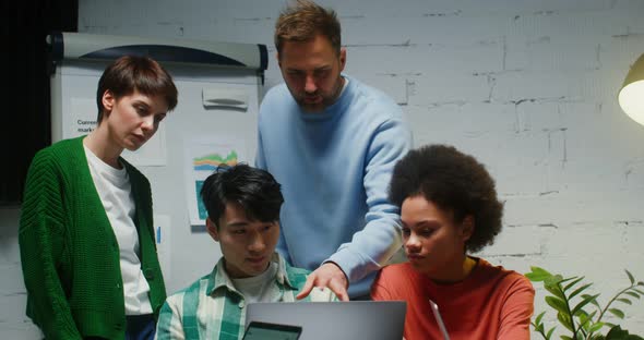 A Group of People Stand Near Workplace of Their Colleague and Look at His Laptop