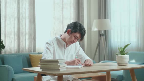Asian Man Student Writing In The Notebook On The Table While Studying At Home