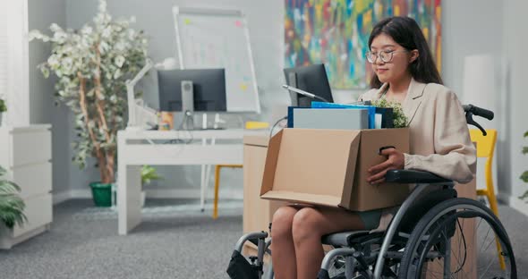 Disabled Woman with Glasses and Asian Korean Beauty Sits in Wheelchair at Corporate Desk on Lap