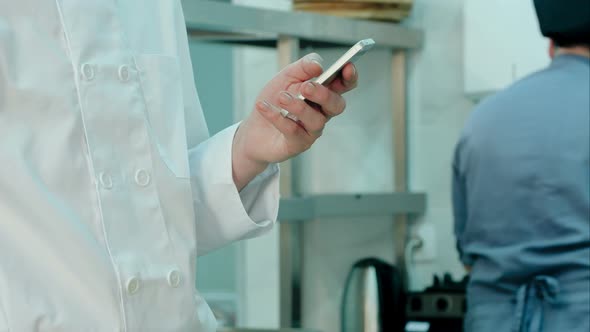 Male Chef's Hands Holding Mobile Phone in the Restaurant Kitchen