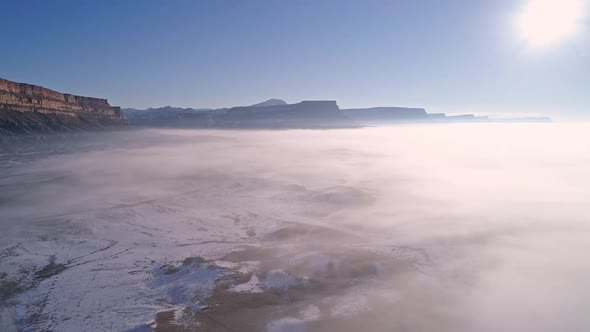 Panning aerial view of thin layer of fog over snow in the desert