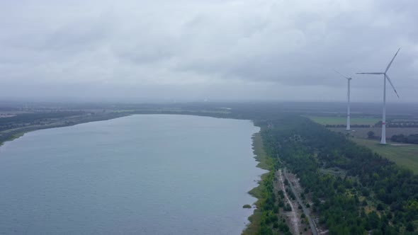 Moving wind turbine to create green wind energy, ituated next to a lake at a cloudy day in aerial vi