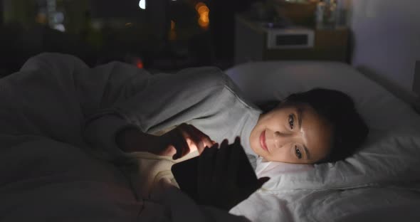 Woman use of cellphone and lying on bed at night