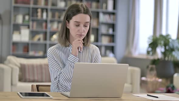 Young Woman Thinking and Working on Laptop in Office