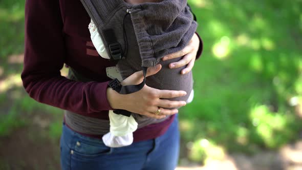 Mom Strokes a Newborn Baby in a Sling