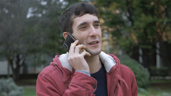 Smiling handsome young man talking by smartphone in the park