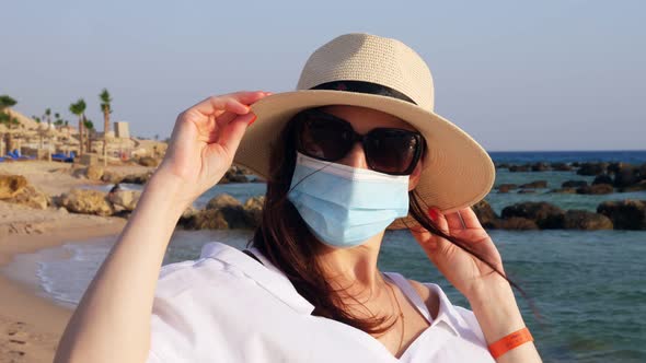 Portrait of Woman in Protective Mask, Sunglasses and Sun Hat, Against Sea Background, Beach