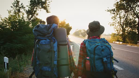 Couple of Tired Backpackers Walking Along Highway Woman Turning to See Moving Car