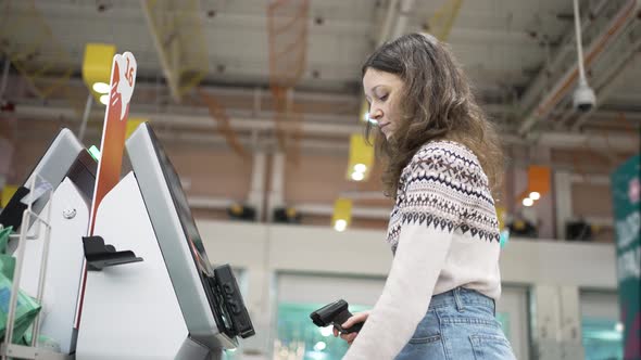 A Young Woman at the Selfservice Checkout in a Grocery Supermarket Makes Purchases