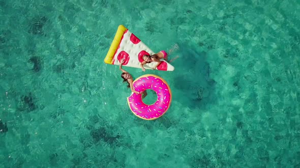 Close aerial view of two young girls swimming and playing in sea with inflatables.