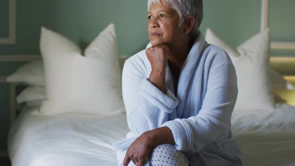 Senior mixed race woman at home sitting on bed thinking