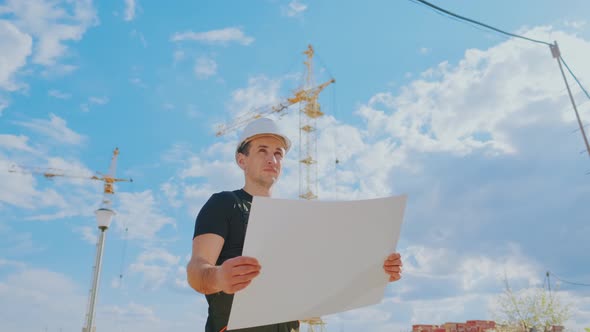 A Man in a Helmet Is Holding a Construction Plan in His Hands