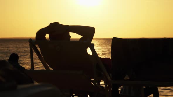 Silhouette of Man Lying on Sun Lounger Looking at the Sunset By Ocean Zanzibar