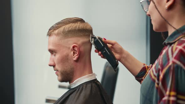 Barbershop: woman hairdresser cuts man's hair with a razor