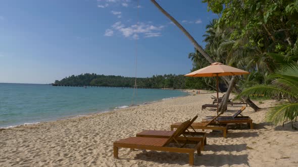 Wide shot of beach beds with umbrella on white sandy beach. Koh Kood, Thailand. TILT DOWN