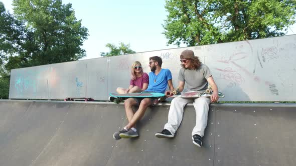 Cool young friends sitting on a ramp at skatepark and chilling