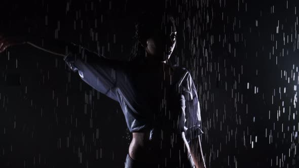 Beautiful girl in a black swimsuit and shirt is standing in the rain, enjoying the drops of water. W