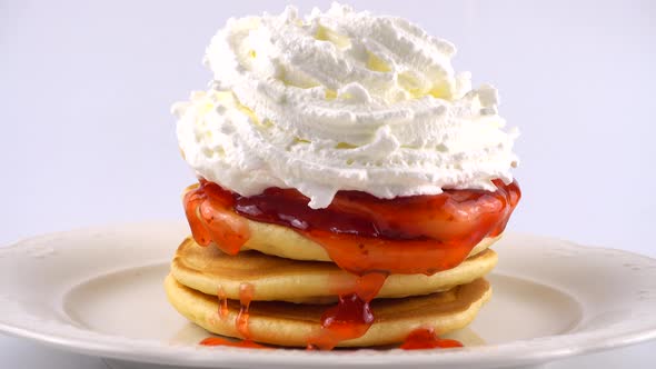 American pancakes with strawberry topping and whipped cream on a white background.