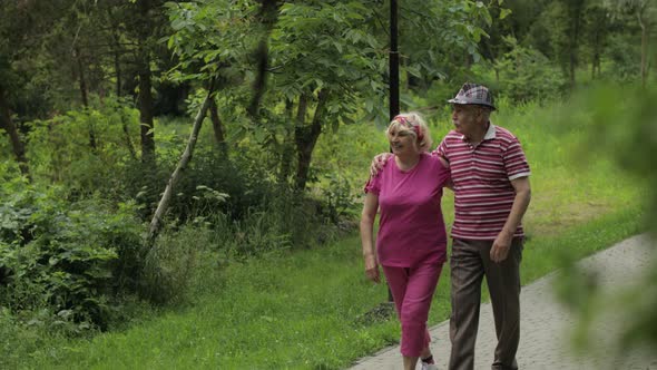 Senior Caucasian Couple Walking in Park Embracing. Elderly Man Walks with Woman. Husband, Wife