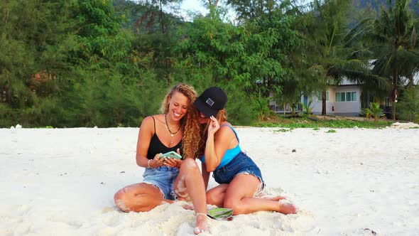 Pretty smiling girls relaxing in the sun at the beach on sunny blue and white sand background 