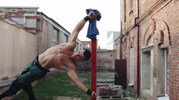 Muscular Topless Young Guy Doing Calisthenics on a Vertical Red Bar Outdoors