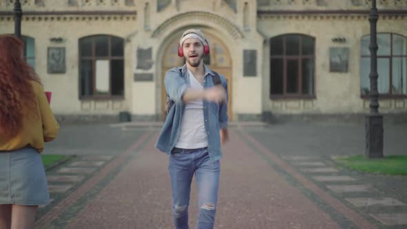 Portrait of Cheerful Relaxed Young Man in Headphones Walking and Dancing As Students Passing at the