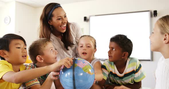 Teacher assisting school kids in reading globe in classroom