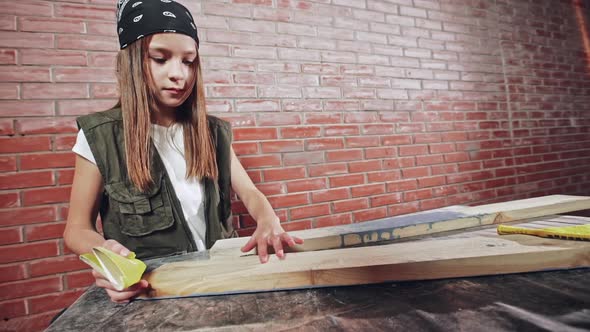 Young Girl in a Bandanna Sanding a Plank of Wood with Handheld Sandpaper During Home Renovations or