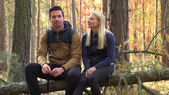 A Hiking Couple Sits on a Broken Tree and Talks in a Forest