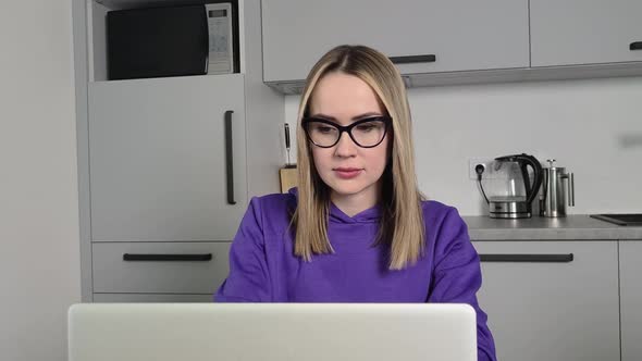 Annoyed Young Adult Woman in Glasses Work Study at Kitchen Using Laptop