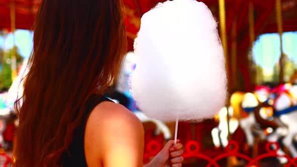 Sad Pensive Young Woman Eating Cotton Candy Carousel in the Background Amusement Park