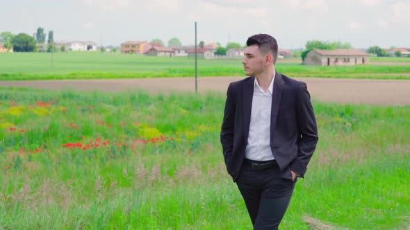 Elegant Guy Walks in Front of the Fields with Green Grass