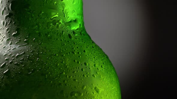 Cooled Wet Green Beer Bottle Rotating Against Black and Grey Background. Beer Bottle with Waterdrops