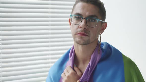 Portrait of Gay Man Wrapped in Rainbow Flag Sitting by Window